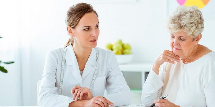 Eine Patientin sitzt mit einer Ernaehrungsberaterin die ihr gerade etwas erklärt am Tisch