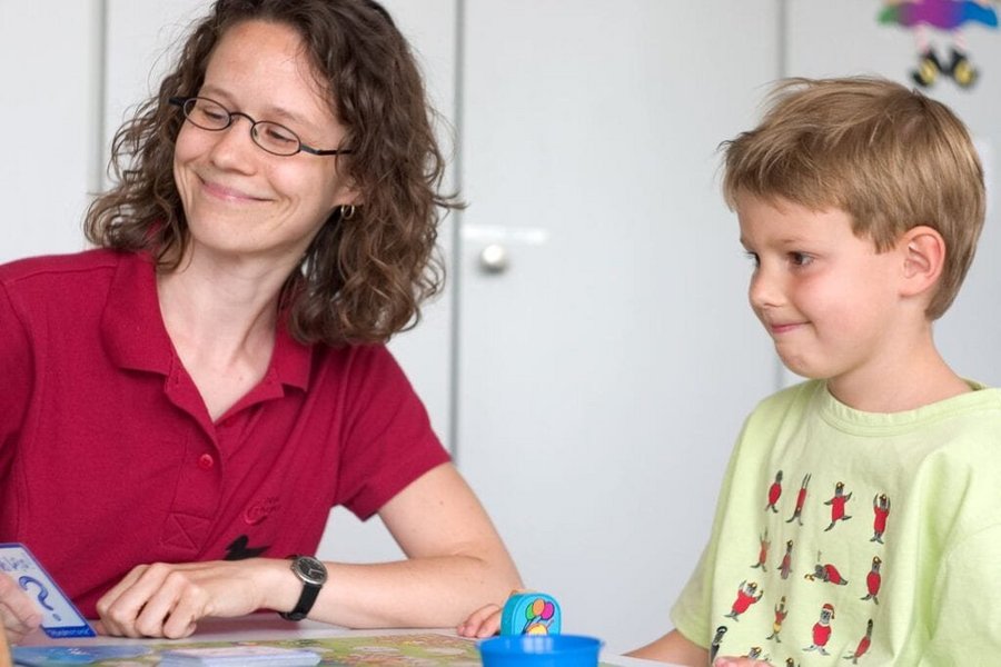Eine Logopaedin uebt Mundmotorik mit einem kleinen Jungen in der Therapie von Sprachentwicklungsstoerung im Praxisbetrieb des VAMED Rehazentrum Karlsruhe