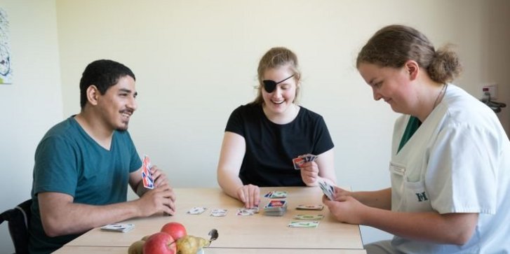Junge Erwachsene und Erzieherin spielen Karten