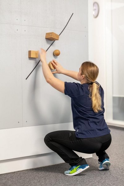 Eine Patientin arbeitet in der Hocke vor einer Wand im Rahmen der medizinisch beruflich orientierten Rehabilitation des VAMED Rehazentrums Karlsruhe