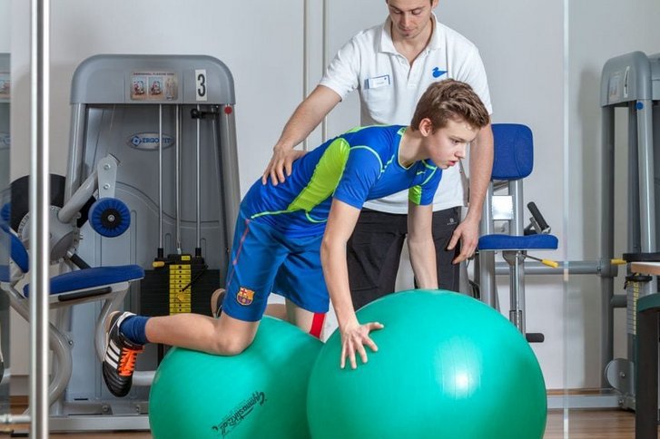 Ein Patient steht durch einen Therapeuten unterstuetzt im Vierfuesslerstand auf zwei Pezzibaellen in der Physiotherapie Karlsruhe