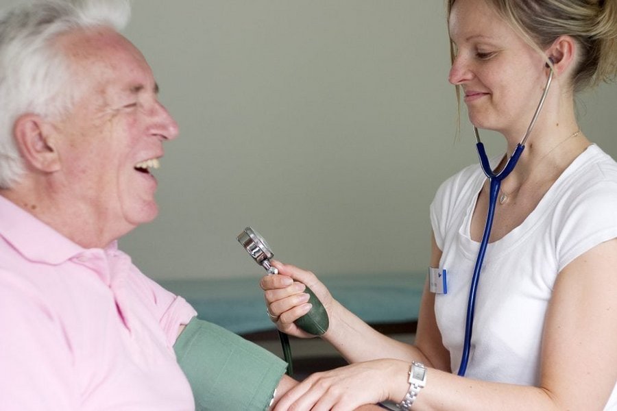 Lachender Patient bekommt von Aerztin Blutdruck gemessen